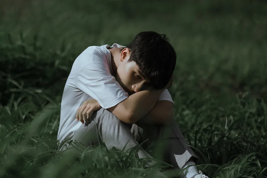 Young man sitting alone on the grass with his head resting on his knees