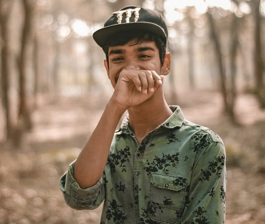 Smiling young man in a cap, covering his mouth shyly