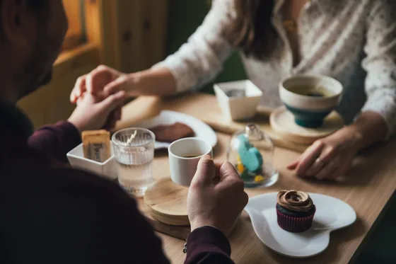 Couple holding hands across a café table with coffee and cupcakes