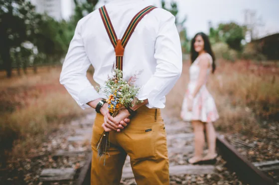 Man hiding a bouquet behind his back as he walks towards a woman