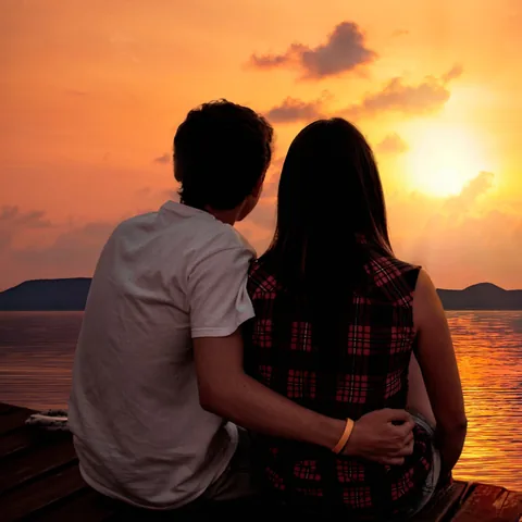 Couple sitting together on a pier, watching the sunset over the water