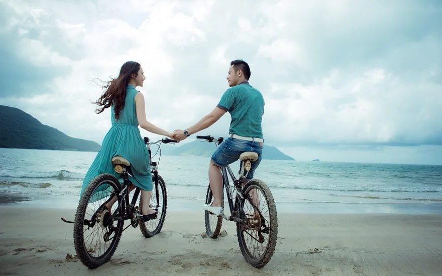 Couple holding hands while cycling along a beach