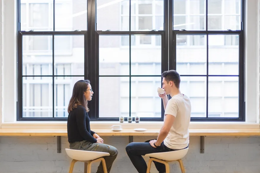 Man and woman talking at a window counter in a bright café